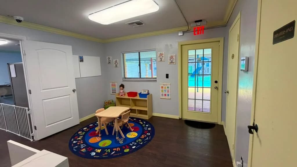 Classroom play corner with alphabet rug, kids table and direct playground access at A Magic World Child Care Center