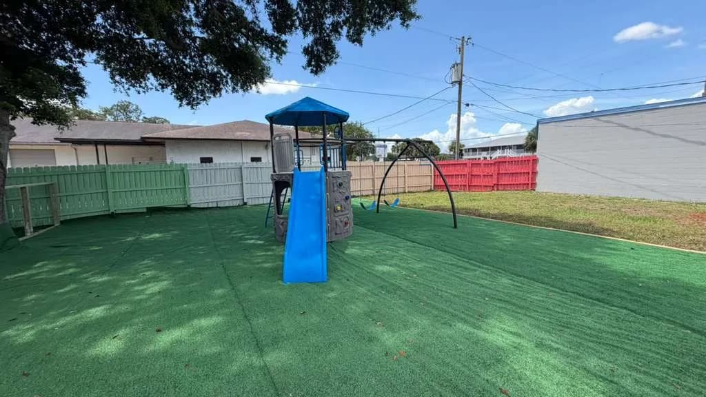 Outdoor playground with blue slide and swings on safe turf at A Magic World Child Care Center in Palm Bay, FL