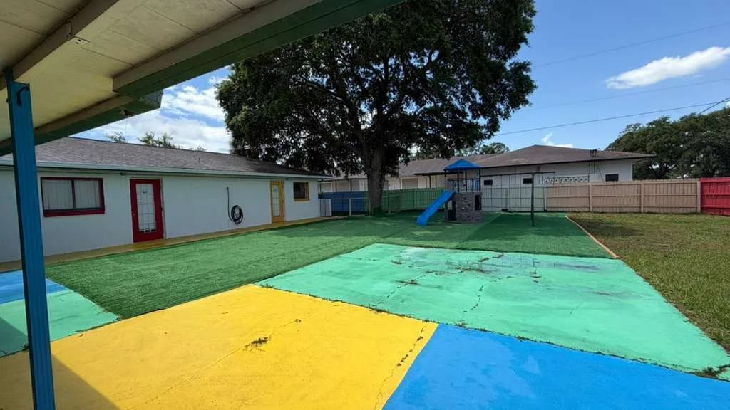 Spacious outdoor play space with shade tree and colorful surfacing at A Magic World Child Care Center
