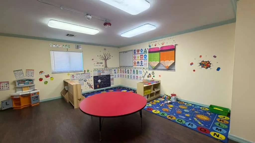 Bright toddler classroom with learning rug and play kitchen at A Magic World Child Care Center